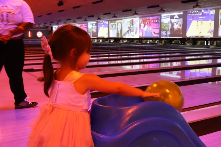 A young bowler in a pink dress rolling her ball