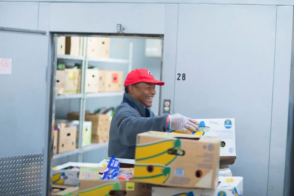 Smiling volunteer in a red cap sorting boxes in the pantry