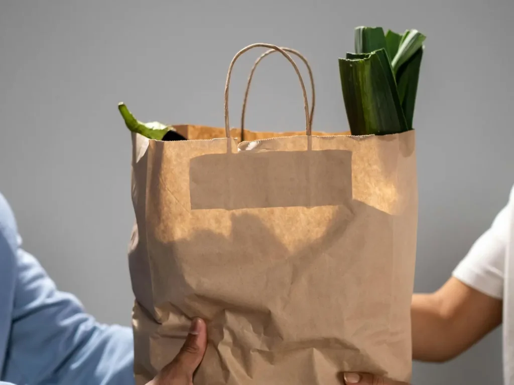 A paper pantry bag of fresh produce being handed from one person to another