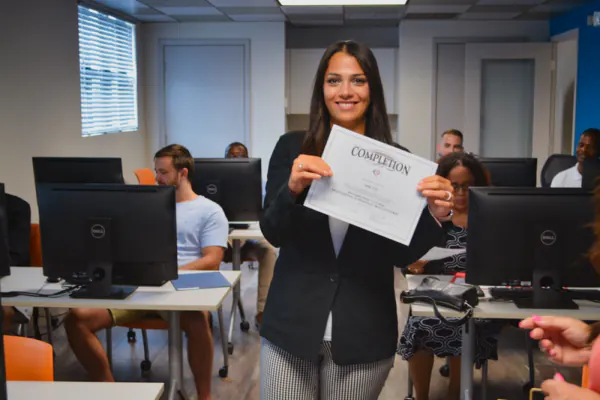 Graduate holding her certificate in a training classroom