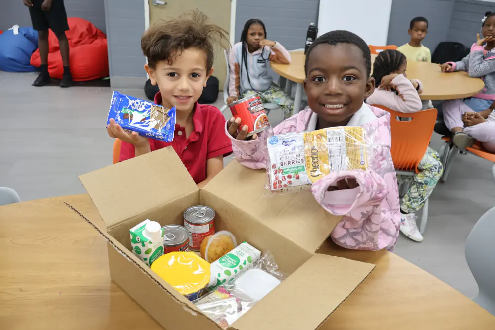 Children holding snacks beside a donation box